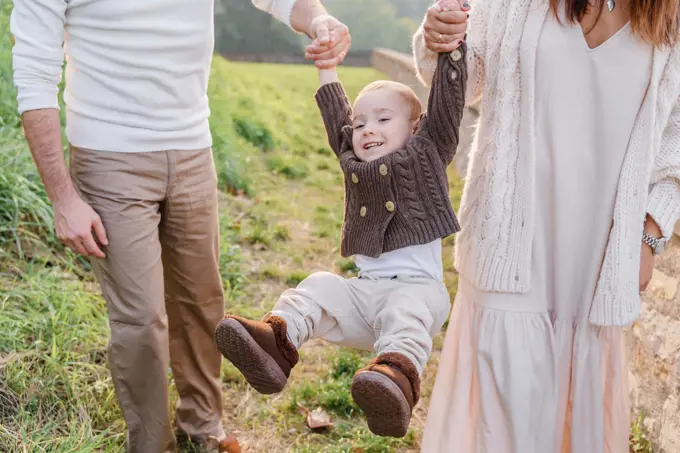 Mom and dad hold the toddler boy by the arms and roll him, he la