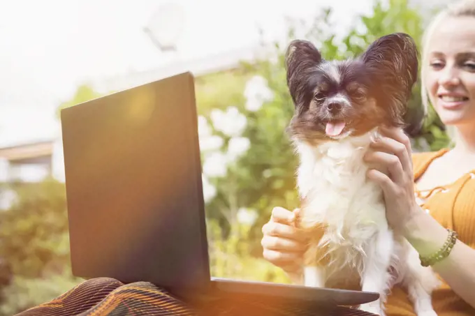 Young woman using laptop with her dog in the domestic garden, Munich, Bavaria, Germany