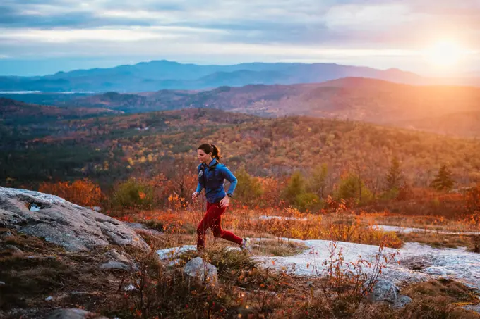 Woman trail running in mountains with foliage in autumn
