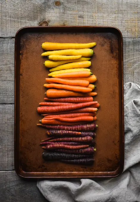 Metal pan of multicoloured carrots on a wooden background.
