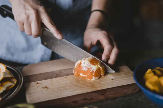 Closeup of hands and knife cutting orange on wooden cutting board