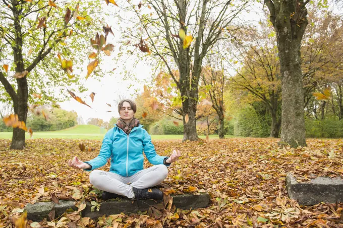 Woman meditating while sitting on a rock in autumn scenery