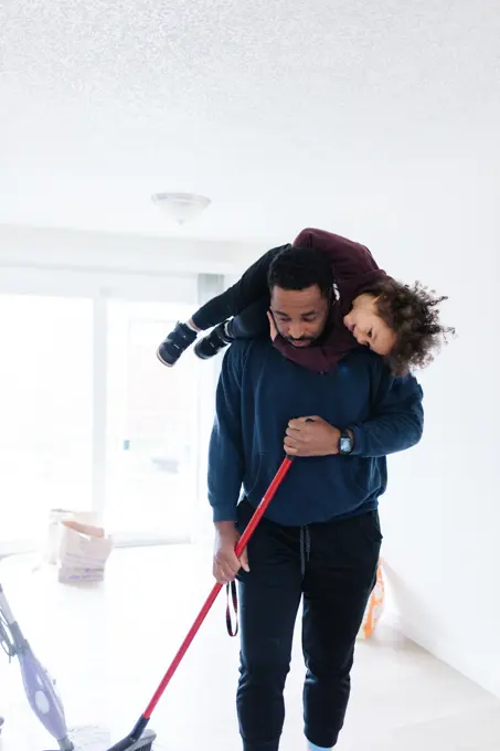 Black father cleaning the house, sweeping, and toddler on shoulders