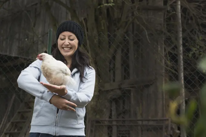 Farmer woman with white chicken bird and smiling in farm, Bavaria, Germany
