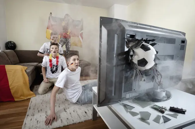 Teenage soccer fans in living room with ball demolishing TV