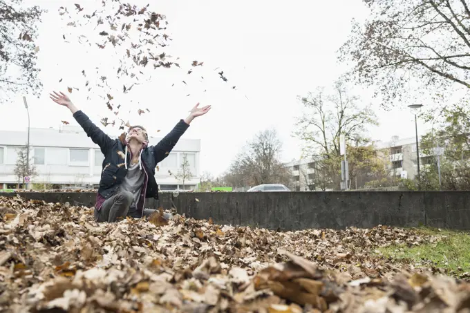 Young man throwing autumn dry leaves in air, Munich, Bavaria, Germany