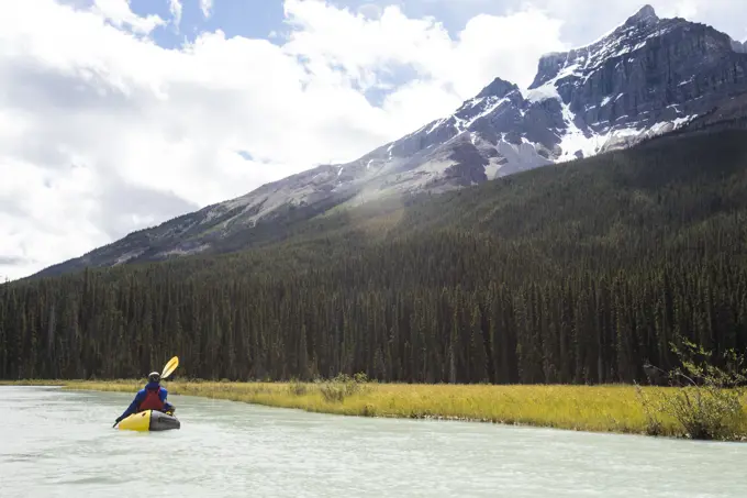 Rear view of person paddling on river below towering mountain summits