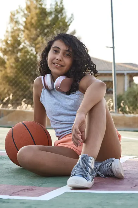 Close-up of a sitting girl with curly hair with a basketball and headphones