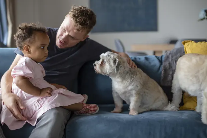 A caucasian father sits with his biracial daughter and puppy