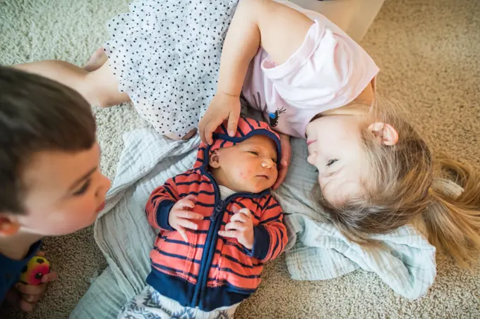 Older brother and sister cuddle their new baby brother.