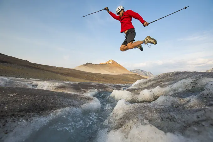 Hiker jumps over glacial stream.