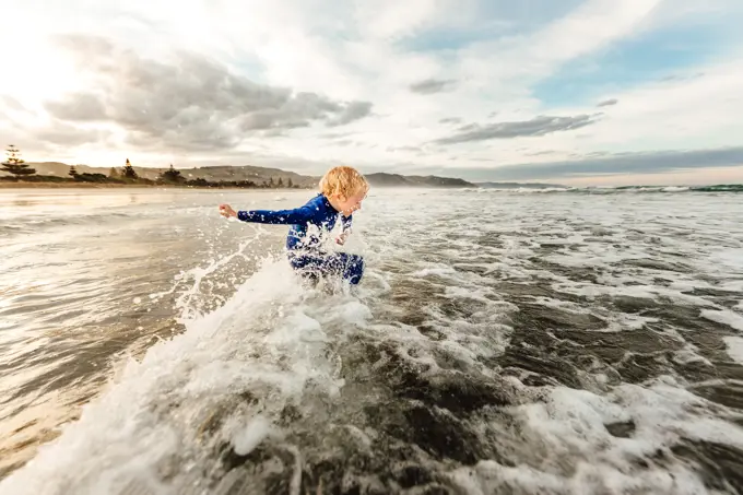 Young child jumping waves at a beach in New Zealand