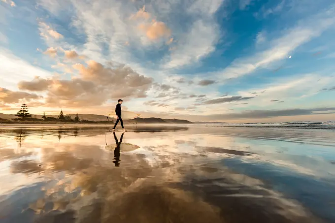 Teen with surfboard on a beach in New Zealand at sunset