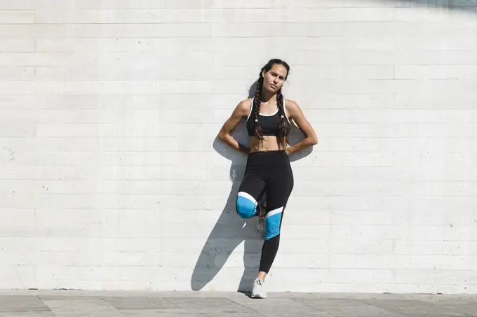 Full body portrait of female athlete leaning on concrete wall