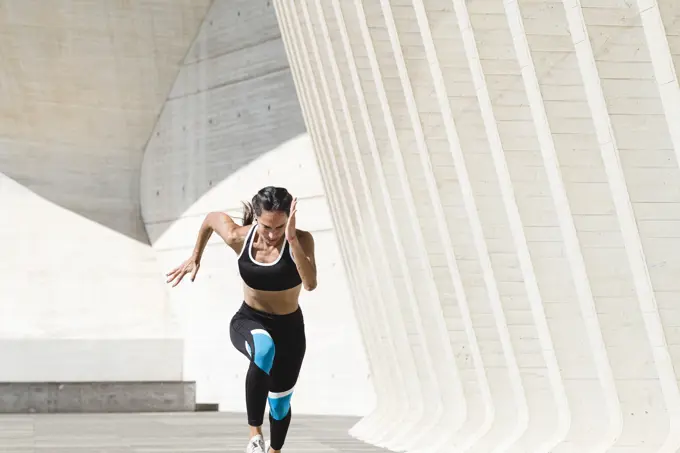 Upper body of female athlete in sportswear running fast on concrete