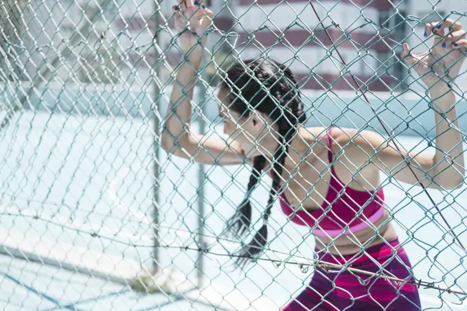 Upper body of female athlete leaning on court fence while resting