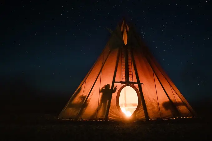 Shadow of people inside glowing teepee lit up under night sky