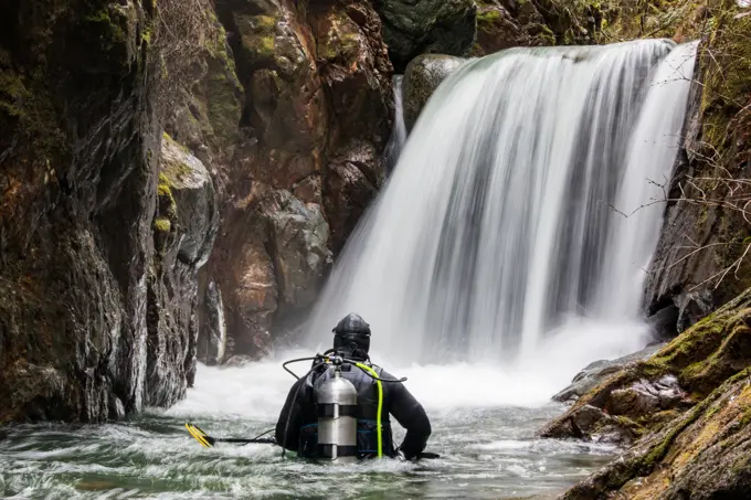 Rear view of scuba diver standing in river looking at waterfall