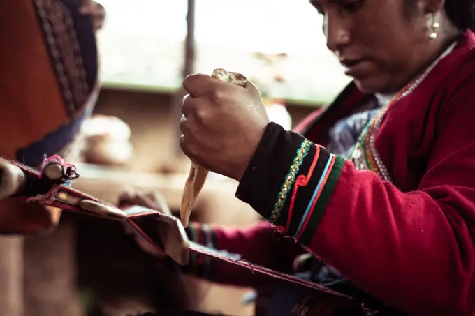 Local woman in traditional clothes weaves alpaca wool with bone