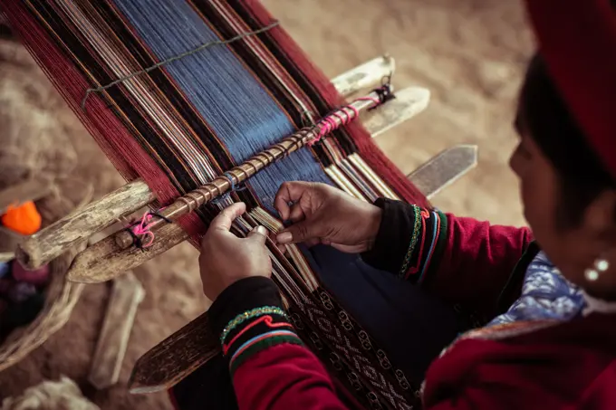 Local woman in traditional clothes weaves alpaca wool with bone