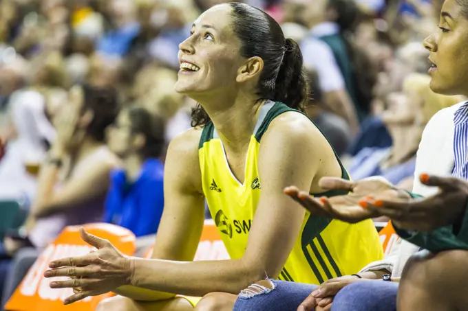 Female athlete sitting on bench smiling and clapping during game, Seattle, Washington, USA