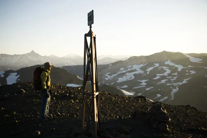 A young man, hiking on the border of Argentina and Chile, greets a rising sun at the marker indicating the border between Chile