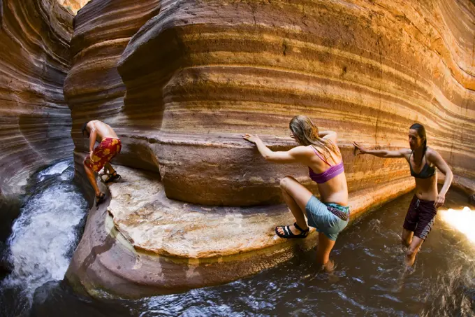 Three people scrambling down a slot canyon with flowing water, Deer Creek, Grand Canyon, Arizona.