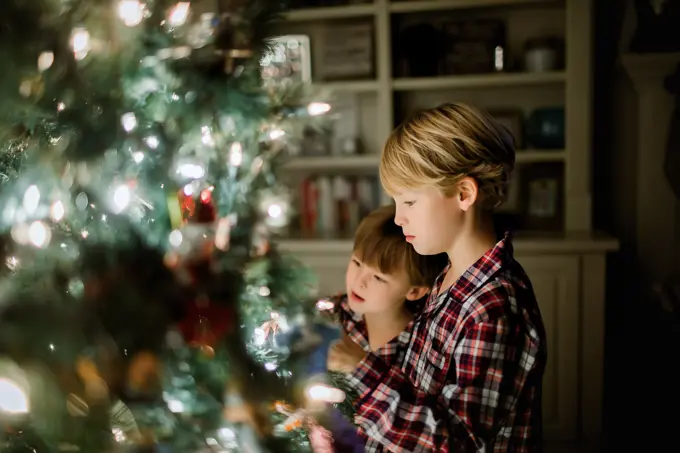 Two boys in plaid pajamas admiring a decorated Christmas tree at