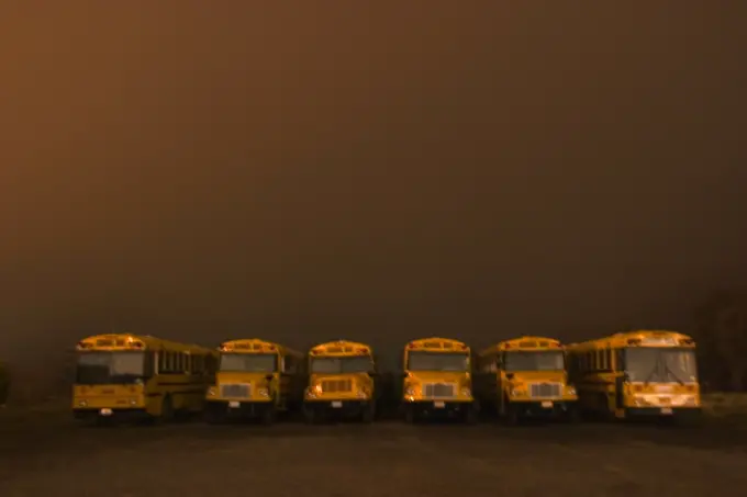 Buses sit in line beneath a brown colored, foggy sky. Auburn California.