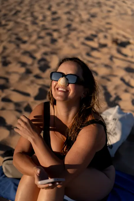 Woman holds a seashell on her nose on the beach.