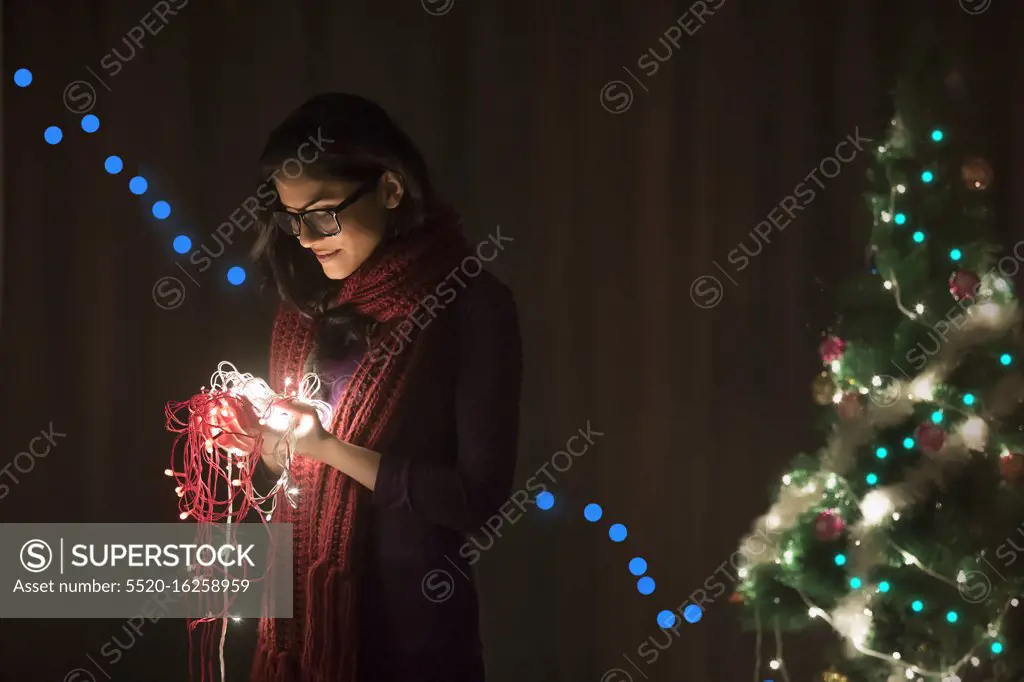 Portrait of a woman holding fairy lights during Christmas celebration.