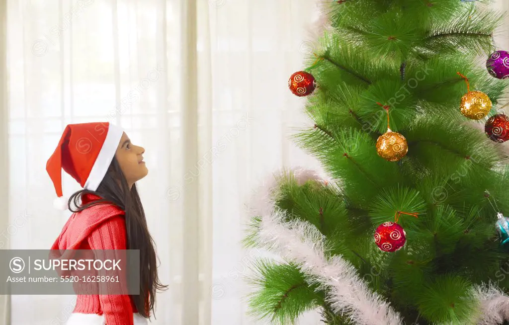 Young girl looking at a Christmas tree at home. (Children)