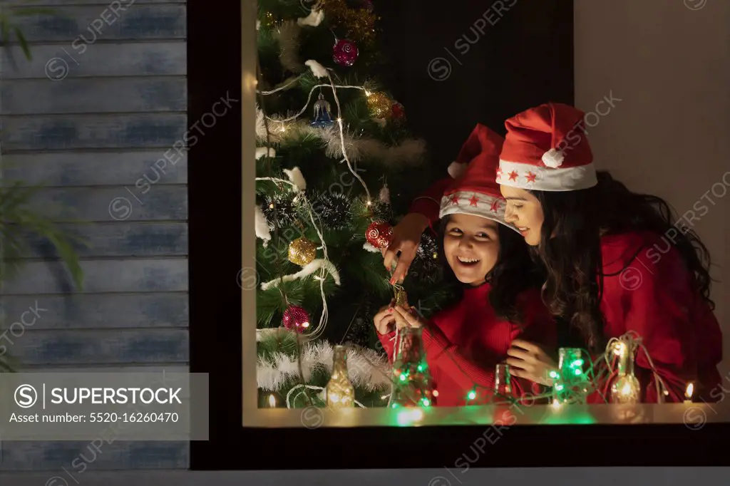 Mother and daughter decorating a Christmas tree inside their home.