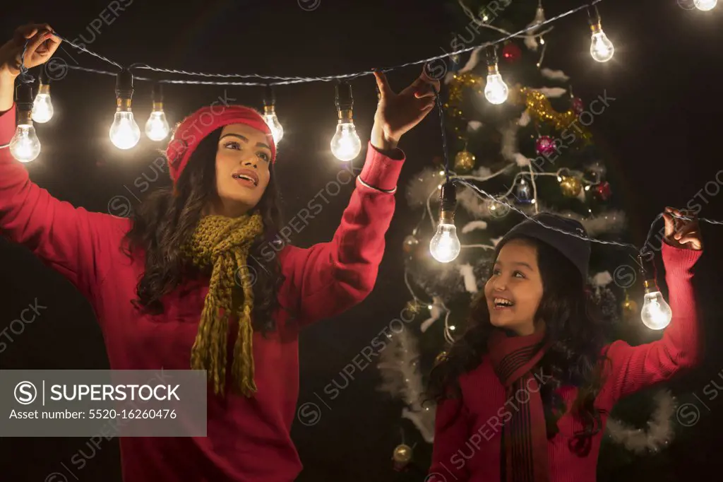 Mother and daughter decorating home with lights during Christmas.