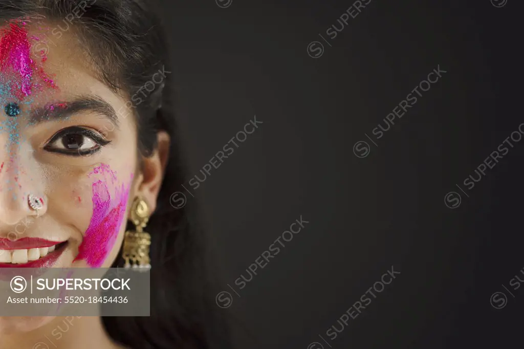 CLOSE SHOT OF ONE SIDE OF A FACE OF A YOUNG WOMAN WITH HOLI COLOURS ON HER