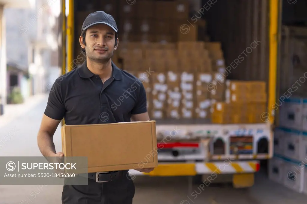 Courier boy standing with a parcel in his hand and smiling