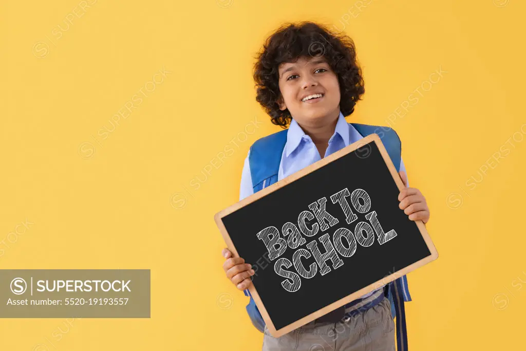 A BOY IN SCHOOL UNIFORM HAPPILY DISPLAYING MESSAGE OF BACK TO SCHOOL AFTER PANDEMIC