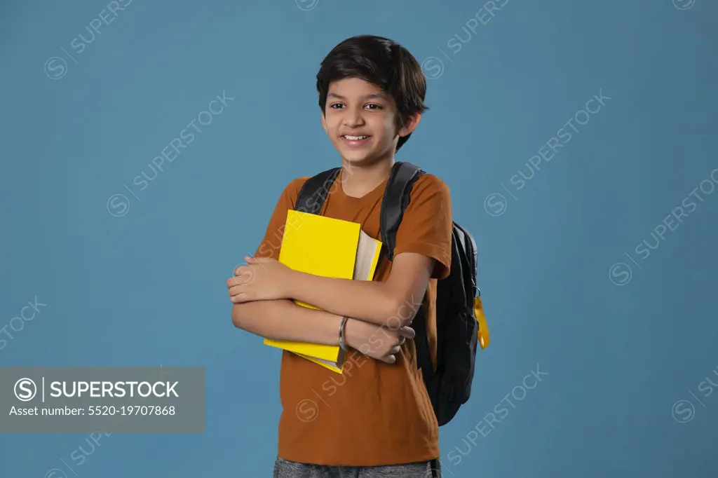 Portrait of smiling boy holding books while standing against blue background