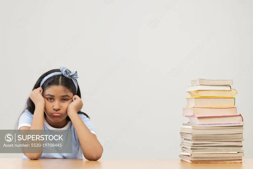 Girl with bored expression sitting beside stack of books 