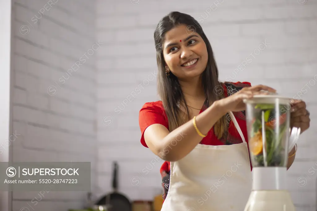 Portrait of smiling woman preparing healthy smoothie in kitchen