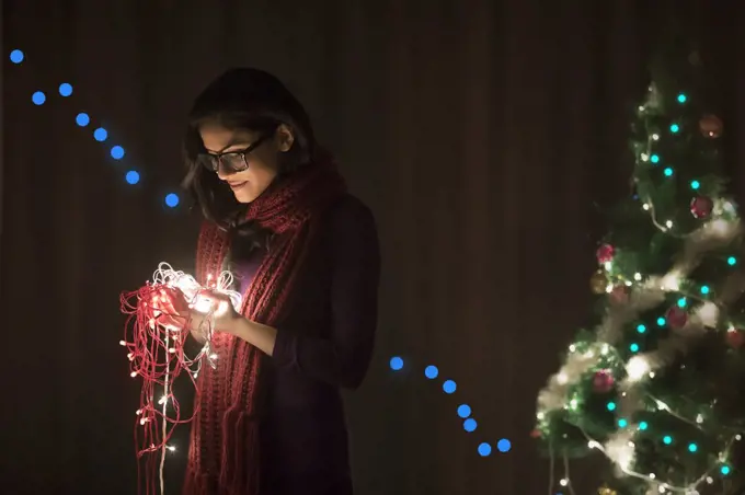 Portrait of a woman holding fairy lights during Christmas celebration.