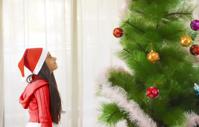 Young girl looking at a Christmas tree at home. (Children)