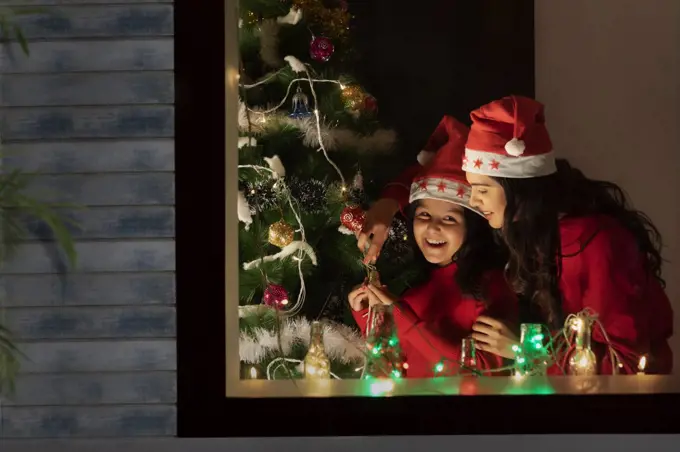 Mother and daughter decorating a Christmas tree inside their home.