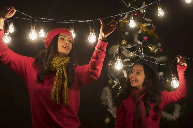 Mother and daughter decorating home with lights during Christmas.