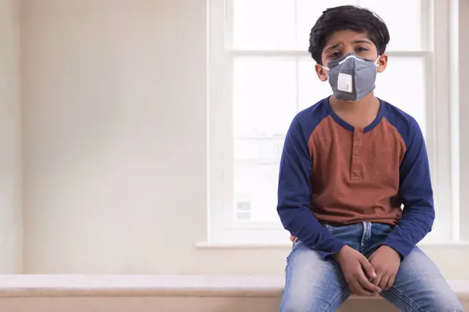 Young boy looking tired of wearing a pollution mask at home. (Children)