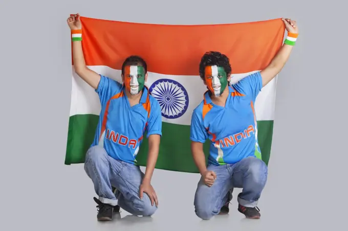 Two male friends with face painted in a tricolor holding Indian flag over colored background