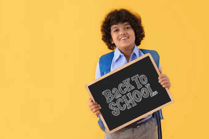 A BOY IN SCHOOL UNIFORM HAPPILY DISPLAYING MESSAGE OF BACK TO SCHOOL AFTER PANDEMIC