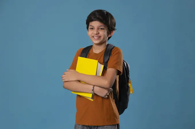 Portrait of smiling boy holding books while standing against blue background