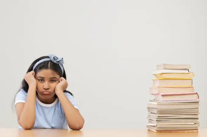 Girl with bored expression sitting beside stack of books 