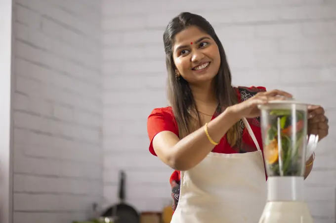 Portrait of smiling woman preparing healthy smoothie in kitchen